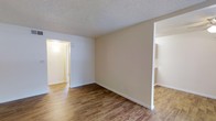 This single-floor unit offers a practical and straightforward layout across a generously sized floor plan. The main living area is open and unobstructed, finished with warm wood-style laminate flooring that extends throughout the space, adding a cohesive and inviting feel underfoot. Neutral beige walls provide a versatile backdrop, making the space easy to personalize with various décor styles.

The textured ceiling adds a classic touch overhead, while white baseboards and door trim provide clean contrast against the walls and flooring. Doorways connect the living area to additional rooms, offering an accessible and efficient flow through the unit. A lit hallway visible from the main area leads to the remaining rooms, suggesting a well-organized interior arrangement.

The layout includes one bedroom and one bathroom, making it well-suited for an individual or couple. The overall design emphasizes simplicity and functionality, with neutral finishes throughout that create a bright, clean environment. The space is move-in ready and provides a solid foundation for comfortable, everyday living.