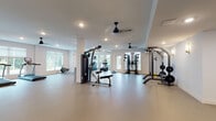 Located at 3125 Fire Ct in Charlotte, NC, this dedicated fitness facility is designed to support a comprehensive range of exercise routines within a bright, open single-floor layout. The space is organized into distinct functional zones, each catering to different training modalities while maintaining a clean, uncluttered aesthetic throughout.

The main workout area is expansive, featuring smooth, durable flooring finished in neutral tones that provide an easy-to-maintain surface suited for both equipment use and open-floor exercises. Recessed lighting is distributed evenly across the ceiling, complemented by ceiling fans that promote air circulation during workouts. Large windows fitted with blinds line multiple walls, inviting generous natural light and offering views of the surrounding greenery.

Cardio equipment includes treadmills, an elliptical trainer, a rowing machine, and a stationary bike, all thoughtfully arranged to maximize open floor space. Strength training is well-represented with a multi-station cable machine, a weight rack stocked with free weights, a barbell rack, a functional training rig with suspension straps, and adjustable benches. Wall-mounted mirrors in the strength area allow users to monitor form during exercises.

A secondary, more intimate room provides additional space for focused strength training, featuring wall sconces, a weight rack, and a barbell station. The overall environment is clean, modern, and functionally designed to support diverse fitness needs.