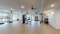 Located at 3125 Fire Ct in Charlotte, NC, this dedicated fitness facility is designed to support a comprehensive range of exercise routines within a bright, open single-floor layout. The space is organized into distinct functional zones, each catering to different training modalities while maintaining a clean, uncluttered aesthetic throughout.

The main workout area is expansive, featuring smooth, durable flooring finished in neutral tones that provide an easy-to-maintain surface suited for both equipment use and open-floor exercises. Recessed lighting is distributed evenly across the ceiling, complemented by ceiling fans that promote air circulation during workouts. Large windows fitted with blinds line multiple walls, inviting generous natural light and offering views of the surrounding greenery.

Cardio equipment includes treadmills, an elliptical trainer, a rowing machine, and a stationary bike, all thoughtfully arranged to maximize open floor space. Strength training is well-represented with a multi-station cable machine, a weight rack stocked with free weights, a barbell rack, a functional training rig with suspension straps, and adjustable benches. Wall-mounted mirrors in the strength area allow users to monitor form during exercises.

A secondary, more intimate room provides additional space for focused strength training, featuring wall sconces, a weight rack, and a barbell station. The overall environment is clean, modern, and functionally designed to support diverse fitness needs.