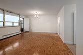 Located on the 16th floor at 2550 Kingston Rd in Toronto's Scarborough area, this suite offers a well-organized layout comprising six rooms, including a living area, bedroom, kitchen, and bathroom. The living room is a standout space, featuring polished parquet wood flooring in a classic herringbone pattern and floor-to-ceiling windows that frame sweeping panoramic views of Lake Ontario, allowing abundant natural light to fill the room. A chandelier adds a touch of elegance overhead. Baseboard heating runs along the exterior walls beneath the windows throughout the unit. The bedroom continues the parquet flooring theme and includes a double closet for ample storage, with its own window offering outdoor views. The kitchen is outfitted with white cabinetry, light stone-finish countertops, tile flooring, and includes a full-sized refrigerator, providing practical and clean workspace. The bathroom features a full soaker tub with a white tiled surround, maintaining a clean and straightforward aesthetic. A balcony is accessible from one of the rooms, extending the living space outdoors. Overall, the unit presents a bright and functional living environment elevated by its remarkable lakefront views.
