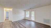 Located in Mechanicsville, Virginia, this single-floor, 2-bedroom, 2-bathroom residence offers a practical and comfortable layout designed for everyday living. The open living room is finished with wood-style plank flooring and neutral walls, complemented by a window and a glass door that invite natural light and provide direct access to the outdoors. Adjacent to the living area, the kitchen features a peninsula with a granite-look countertop and double sink, warm honey-toned cabinetry, white appliances including a refrigerator and range, and a textured ceiling throughout. A dedicated laundry area is conveniently tucked within the unit. The primary bedroom is generously sized, carpeted for comfort, and benefits from two windows overlooking green outdoor views. The second bedroom is also carpeted and offers a cozy, versatile space. Both bathrooms are clean and functional — one features a wood-vanity with an oversized mirror and shower, while the other includes a full soaking tub with surround. Two closets provide ample storage throughout the home. The consistent use of light, neutral tones and wood-style flooring in common areas gives the residence a cohesive and inviting character.