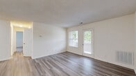 Located in Mechanicsville, Virginia, this single-floor, 2-bedroom, 2-bathroom residence offers a practical and comfortable layout designed for everyday living. The open living room is finished with wood-style plank flooring and neutral walls, complemented by a window and a glass door that invite natural light and provide direct access to the outdoors. Adjacent to the living area, the kitchen features a peninsula with a granite-look countertop and double sink, warm honey-toned cabinetry, white appliances including a refrigerator and range, and a textured ceiling throughout. A dedicated laundry area is conveniently tucked within the unit. The primary bedroom is generously sized, carpeted for comfort, and benefits from two windows overlooking green outdoor views. The second bedroom is also carpeted and offers a cozy, versatile space. Both bathrooms are clean and functional — one features a wood-vanity with an oversized mirror and shower, while the other includes a full soaking tub with surround. Two closets provide ample storage throughout the home. The consistent use of light, neutral tones and wood-style flooring in common areas gives the residence a cohesive and inviting character.