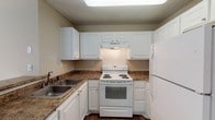 Located at 2945 Layfair Dr in Flowood, Mississippi, this single-floor residence offers a well-organized layout designed for comfortable everyday living. The kitchen is efficiently arranged in a U-shaped configuration, featuring white cabinetry, granite-style countertops, wood-look flooring, a double-basin sink, an electric range, and a full-size refrigerator. A skylight overhead brings additional brightness to the cooking space. The kitchen opens toward a combined living and dining area, where plush carpeting, neutral warm-toned walls, and a pendant light fixture create an inviting atmosphere. A large sliding glass door in the living area provides access to the outdoors and allows natural light to fill the room. Bedrooms are carpeted and finished with the same neutral tones, each offering closet storage — one with a walk-in closet and another with a standard reach-in closet with built-in shelving. The primary bathroom includes a single-sink vanity with granite-style countertops, white cabinetry, a lighted mirror, and wood-look flooring. A second full bathroom mirrors this aesthetic and includes a shower-tub combination. Textured ceilings are consistent throughout, contributing to the cohesive character of the space.