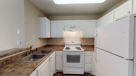 Located at 2945 Layfair Dr in Flowood, Mississippi, this single-floor residence offers a well-organized layout designed for comfortable everyday living. The kitchen is efficiently arranged in a U-shaped configuration, featuring white cabinetry, granite-style countertops, wood-look flooring, a double-basin sink, an electric range, and a full-size refrigerator. A skylight overhead brings additional brightness to the cooking space. The kitchen opens toward a combined living and dining area, where plush carpeting, neutral warm-toned walls, and a pendant light fixture create an inviting atmosphere. A large sliding glass door in the living area provides access to the outdoors and allows natural light to fill the room. Bedrooms are carpeted and finished with the same neutral tones, each offering closet storage — one with a walk-in closet and another with a standard reach-in closet with built-in shelving. The primary bathroom includes a single-sink vanity with granite-style countertops, white cabinetry, a lighted mirror, and wood-look flooring. A second full bathroom mirrors this aesthetic and includes a shower-tub combination. Textured ceilings are consistent throughout, contributing to the cohesive character of the space.