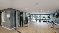 Located at 427 Blue Ridge Drive in Augusta, Georgia, this single-story fitness facility offers a thoughtfully organized layout designed to support a wide range of exercise activities. The space is spread across one floor and is divided into distinct functional areas connected by two hallways.

The main exercise room is generously proportioned and finished with light wood-look flooring that contributes to a clean, modern aesthetic. Dark slate-blue accent walls provide a bold contrast against the white ceiling, which features recessed lighting for consistent illumination throughout. Large windows and glass doors line the perimeter, flooding the space with natural light and offering views of the surrounding greenery. The room is equipped with a Precor cable machine, a full dumbbell rack, weight benches, treadmills, ellipticals, and a stationary bike, along with a wall-mounted television. Full-length mirrors are strategically placed to maximize sightlines across the floor.

A secondary studio room features a wall-to-wall mirror with a mounted wooden ballet barre and light wood flooring, making it well-suited for barre, yoga, or Pilates classes. Stability balls are stored along the perimeter, and track lighting overhead ensures even coverage. An additional flexible room with a pass-through window overlooking the main gym provides a quieter, adaptable space within the facility.