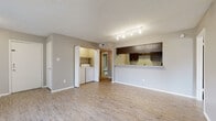 This single-floor unit offers a functional and cohesive layout highlighted by light-toned wood-style flooring that runs throughout the entire space. The open living area is generously sized, bathed in natural light from a large sliding glass door that leads to a private patio. A corner fireplace adds a focal point to the living room, while track lighting overhead provides ample illumination. In-unit laundry is conveniently located within the living area, tucked behind cabinetry with overhead storage.

The kitchen connects to the living space via a raised pass-through bar with granite-style countertops, offering both functionality and an open sightline. Dark espresso cabinetry contrasts with light counters, and the kitchen is equipped with black appliances including an electric range, over-the-range microwave, and refrigerator. Textured walls add a subtle dimension to the interior throughout.

The bedroom is a quiet, comfortable space featuring a window with natural views and blinds for privacy. The unit includes two bathrooms: one with a granite-topped vanity, dark wood-framed mirror, and wood-style flooring, and another with a full tiled tub/shower combination. The textured ceiling is consistent throughout, tying the space together with a cohesive, residential aesthetic.