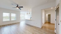 This well-appointed single-floor residence offers 1 bedroom and 2 bathrooms within a thoughtfully designed open-concept floor plan. Light wood-tone flooring flows consistently throughout the space, complemented by crisp white walls and clean modern finishes that create a bright, airy atmosphere.

The combined kitchen and living area serves as the heart of the home. The kitchen features a peninsula with a matte black faucet and sink, illuminated by a pair of stylish cone-shaped pendant lights. A stainless steel refrigerator and white cabinetry with decorative wine rack detailing complete the kitchen. The adjacent living area is bathed in natural light from multiple windows and is equipped with a ceiling fan.

The bedroom is generously sized, featuring dual windows that frame outdoor views of palm trees and greenery, along with its own ceiling fan. Two closets provide ample storage throughout the unit. A hallway connects the private areas of the home, leading to two bathrooms finished with light wood flooring and matte black hardware accents.

A dedicated laundry room includes an in-unit washer and overhead wire shelving for added convenience. The overall design of this residence emphasizes clean lines, natural light, and a cohesive modern aesthetic.