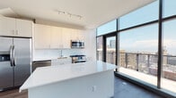 Located along South Federal Street in Chicago's vibrant South Loop neighborhood, this contemporary multi-floor residence showcases a clean, modern aesthetic throughout. The open-concept kitchen is a standout feature, equipped with stainless steel appliances including a gas range, built-in microwave, and dishwasher, complemented by crisp white cabinetry, a white quartz waterfall island, and track lighting overhead. Dramatic floor-to-ceiling windows flood the living areas with natural light while framing impressive views of the Chicago skyline and Lake Michigan beyond, with access to an outdoor balcony. Dark hardwood-style flooring runs throughout the main living spaces, creating a refined contrast against the bright white walls and ceilings. Exposed concrete ceiling details in portions of the living area add an industrial character consistent with the building's modern architectural identity. The bathrooms are finished with clean-lined dark wood vanities, white quartz countertops, large wall mirrors, and neutral tile flooring. The primary bath features a double-sink vanity and a tiled walk-in shower. Bedrooms are generously proportioned with ample wall space and continued hardwood-style flooring. The two-floor layout offers well-defined living zones, making this Chicago residence both functional and visually striking.