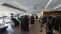 Located at 600 S Wells St in Chicago's vibrant South Loop neighborhood, this upscale fitness center offers a thoroughly equipped, multi-zone workout facility designed for serious training. The space is organized into distinct functional areas, each thoughtfully appointed to support a full range of fitness activities.

The cardio zone features a row of modern treadmills positioned alongside floor-to-ceiling windows that flood the area with natural light and frame striking views of the Chicago skyline. Roller shades allow for adjustable light control throughout the day.

The main strength training floor is outfitted with a comprehensive selection of Technogym machines, including cable systems, multi-functional racks, and resistance equipment, all finished in a sleek black aesthetic. A dedicated free weights section provides dumbbell racks alongside benches, set against rich, dark wood-paneled accent walls that lend warmth and sophistication to the space.

A separate functional training area features open floor space with plyo boxes and additional equipment for dynamic workouts. Glass partitions define zones while maintaining an open, airy feel throughout. Large mirrors amplify the sense of space and aid in form monitoring.

Ceiling fans and linear LED lighting are integrated throughout, providing both comfort and a polished, contemporary ambiance. The overall design balances high performance functionality with refined, modern aesthetics.