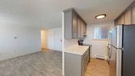 This single-floor unit offers a practical and clean layout designed for comfortable everyday living. The entryway opens into a bright living area finished with light wood-style luxury vinyl flooring, a textured ceiling, and a wall-unit air conditioner alongside baseboard heating. Multiple windows dressed with horizontal blinds allow natural light to filter throughout the space.

The galley-style kitchen is efficiently arranged with gray shaker-style cabinetry spanning both upper and lower sections, white countertops, and stainless steel appliances including a refrigerator and electric range. A pass-through column separates the kitchen from the living area while maintaining an open, connected feel.

The bedrooms are carpeted in a warm neutral tone, each featuring a ceiling fan with a built-in light fixture, baseboard heating, and windows that bring in natural light. The rooms offer a quiet, comfortable atmosphere well-suited for rest.

The bathroom includes a full tub and shower combo with clean white tile surround and a window that provides natural ventilation and light.

Throughout the unit, the design is straightforward and well-maintained, with consistent finishes that create a cohesive and move-in ready environment. Baseboard heating is present in multiple rooms, adding a reliable and consistent climate control option across the unit.