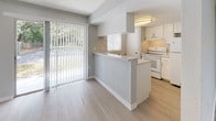 This well-appointed single-floor unit offers a clean, open-concept layout designed for comfortable everyday living. Light wood-style flooring flows consistently throughout the space, complemented by soft grey walls and crisp white trim, creating a bright and cohesive aesthetic.

The living area is generously sized, bathed in natural light through large windows fitted with vertical blinds that offer views of lush greenery outside. A textured ceiling adds dimension to the room, while the open feel allows for flexible furniture arrangements.

The kitchen is efficiently designed with white cabinetry, white appliances, and a peninsula breakfast bar that provides additional counter space and casual seating. A window above the sink brings in natural light, and a sliding glass door connects the kitchen area directly to an outdoor space, enhancing the sense of openness.

The bedroom is spacious and well-lit, featuring a ceiling fan and an impressive dual-closet configuration, offering ample storage for everyday needs. The bathroom is cleanly finished with a full tub-shower combination, white tile surround, and light stone-toned countertop surfaces.

Throughout the unit, the consistent use of neutral tones, natural light, and practical design details make this a functional and inviting space.