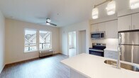 This single-floor unit presents a clean, contemporary design highlighted by an open-concept layout that seamlessly connects the kitchen and living area. The kitchen is well-appointed with stainless steel appliances, including a range, microwave, and refrigerator, complemented by light-toned cabinetry and a white countertop island with an undermount sink. Pendant lighting above the island adds a modern touch, while recessed lighting ensures the space remains bright and functional.

The living area benefits from large windows that invite natural light and offer views of the surrounding neighborhood. A ceiling fan with an integrated light fixture provides both comfort and additional illumination. A glass-paneled exterior door opens to a small balcony, further enhancing the connection to the outdoors.

The bedroom is a well-proportioned, calm retreat featuring a ceiling fan, a sizable window for natural light, and the same warm wood-look flooring found throughout the unit. The bathroom is efficiently designed with a single-sink vanity topped in white, a large mirror, overhead cabinetry for storage, and accessible grab bars near the shower area. Light wood-look flooring ties the bathroom's aesthetic to the rest of the unit, creating a cohesive, modern feel.