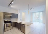 Located at 6055 NW 105th Ct in Doral, FL, this single-floor residence offers a contemporary design with clean lines, neutral tones, and quality finishes throughout. The open-concept kitchen is a standout feature, showcasing high-gloss dark cabinetry, light granite countertops, a large peninsula with an undermount sink, and a full suite of stainless steel appliances including a refrigerator, electric range, microwave, and dishwasher. Pendant lighting and a track lighting system illuminate the space, which flows seamlessly into the living area. Large floor-to-ceiling windows with vertical blinds allow generous natural light to fill the living space, offering views to the outdoors. Light-toned large-format tile flooring runs through the main living areas, while the bedrooms feature plush carpet and ceiling fans. Each bedroom is well-proportioned with natural light provided by window blinds. The primary bathroom is appointed with a granite vanity, tile flooring, and a glass-enclosed walk-in shower, while the secondary bathroom features a matching granite vanity and a tub-shower combination. A dedicated laundry area with a stacked washer and dryer and adjacent shelved storage closet adds everyday convenience to this well-appointed Doral residence.