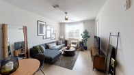 This well-appointed single-floor residence showcases a thoughtfully designed open-concept layout that seamlessly connects the kitchen, dining, and living areas. The kitchen is a standout feature, equipped with stainless steel appliances including a French door refrigerator, built-in microwave, and range. Rich wood-toned cabinetry extends to the ceiling, complemented by granite countertops and a peninsula island with bar seating and elegant pendant lighting overhead — ideal for both casual dining and entertaining. Light wood-style flooring flows throughout the main living area, enhancing the bright and airy atmosphere. The living room offers a generous layout anchored by a sectional sofa, ceiling fan, and curated gallery wall, with windows that bring in natural light. The bedroom provides a cozy retreat with plush carpeting, a ceiling fan, and a window with outdoor views. The bathroom is finished with granite countertops, warm wood cabinetry, a soaking tub with shower, and backlit mirrors that add a contemporary touch. Neutral tones and modern finishes are carried consistently throughout the space, creating a cohesive and inviting ambiance from room to room.