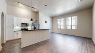 This well-appointed 2-bedroom, 2-bathroom unit showcases a contemporary design with an open-concept layout that seamlessly connects the kitchen and living area. The kitchen is a standout feature, equipped with stainless steel appliances including a French door refrigerator, electric range, and built-in microwave. White shaker cabinetry, a subway tile backsplash, and a dark granite-topped island with a modern industrial-style faucet complete the space. Stylish conical pendant lights hang above the island, complementing the track lighting overhead. The living area is bright and spacious, featuring large windows that invite natural light and durable wood-style flooring that extends throughout the main living spaces. Notably, an exposed metallic HVAC duct and a decorative arched alcove add distinctive architectural character to the room. Both bedrooms are carpeted and feature soaring ceilings, generous closet space, and access to hallways that connect to the bathrooms. Each bathroom is finished with dark granite vanity countertops, white cabinetry, wood-style tile flooring, and a tiled tub-and-shower combination framed by an elegant arched enclosure. A dedicated closet provides additional storage within this thoughtfully designed unit.