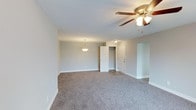 This single-floor space in Rolling Hills offers a bright, open layout designed for comfortable everyday living. The main living area is finished with plush wall-to-wall carpeting in a warm neutral tone, providing a soft and inviting atmosphere throughout. Smooth, light-painted walls and crisp white baseboards contribute to the clean, understated aesthetic of the space.

Overhead, a ceiling fan with an integrated light fixture provides both practical ventilation and ambient lighting, while a pendant light adds a decorative touch that helps define the open area. The transition to adjacent spaces is marked by a shift to hard-surface flooring, visible near the doorways, offering functional contrast to the carpeted living zone.

The layout includes multiple doorways leading to additional rooms or storage areas, including what appears to be a closet with bi-fold doors, suggesting organized storage options. The neutral color scheme throughout creates a versatile canvas that adapts easily to a variety of interior styles. Overall, the space presents a tidy, move-in-ready environment with a calm, understated ambiance well-suited to a range of lifestyles.