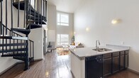 Located at 117 27th Ave SE in Minneapolis, this 2-bedroom, 2-bathroom residence makes a strong architectural impression with its soaring double-height ceilings in the main living area, flooding the space with natural light through stacked windows. The open-concept layout seamlessly connects the kitchen, dining, and living areas, creating an efficient yet airy feel. A sleek spiral staircase serves as a dramatic focal point and adds a modern industrial touch.

The kitchen is equipped with dark cabinetry, granite countertops, stainless steel appliances including a full-size refrigerator, and a peninsula with bar seating — ideal for both cooking and casual dining. The living room benefits from large windows with neighborhood views and warm wood-look flooring that flows throughout the main areas.

Both bedrooms are comfortably sized, with the primary bedroom offering a large window with outdoor views and a double-door closet for generous storage. Each bedroom features light-toned flooring and clean, neutral walls. The two bathrooms are consistently appointed with dark vanity cabinets, granite countertops, and shower/tub combinations. A connecting hallway ties all rooms together efficiently. This well-designed residence offers a modern urban living experience in the heart of Minneapolis.