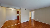 This single-floor residence offers a practical and cohesive layout with warm hardwood-style flooring that extends consistently throughout the living spaces. The main living area is open and well-proportioned, featuring neutral beige walls, a textured popcorn ceiling, and a large window fitted with blinds that allows natural light to fill the room. A front entry door provides direct access to this space.

Adjacent to the living area is a dining nook equipped with a ceiling fan and direct sightlines into the kitchen, creating a connected and functional flow between spaces. The galley-style kitchen is efficiently designed, featuring rich dark cherry wood cabinetry, granite-look countertops, a stainless steel sink, white appliances including an electric range and refrigerator, and a classic white subway tile backsplash. Light hardwood-style flooring continues into the kitchen, maintaining visual continuity.

A bedroom offers a comfortable, carpeted-free environment with the same warm flooring, neutral walls, a window with exterior views, and a textured ceiling. The bathroom includes a combined tub and shower, a toilet, a vanity with storage, and a large mirror. The space as a whole presents a clean, functional interior with consistent finishes and a straightforward, easy-to-navigate single-level floor plan.