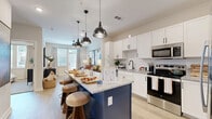 Located in Sugar Hill, GA, this one-bedroom, two-bathroom residence offers a thoughtfully designed single-floor layout that maximizes comfort and functionality. The open-concept kitchen is a standout feature, showcasing crisp white shaker cabinetry with matte black hardware, granite countertops, a striking navy blue island with bar seating, and a full suite of stainless steel appliances including a refrigerator, range, microwave, and dishwasher. Subway tile backsplash and industrial-style pendant lighting add a modern, polished touch. The kitchen flows seamlessly into the living room, which is bathed in natural light from large windows and a glass door that opens to the outdoors. Light wood-look flooring runs throughout the main living areas, creating a warm, cohesive aesthetic. The bedroom offers plush carpeting, a ceiling fan, and generous window exposure for abundant natural light. The two bathrooms are finished with granite-topped vanities and tile surround showers. The primary bathroom connects directly to a dedicated closet that also houses a stacked washer and dryer, adding everyday convenience. Neutral tones and clean lines throughout give the space a contemporary, welcoming ambiance.
