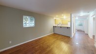 Located at 10124 9th Ave, E117 in Everett, Washington, this single-floor unit offers a practical and comfortable layout with consistent hardwood flooring throughout the living spaces. The open-concept living and dining area is bright and welcoming, featuring warm-toned wood floors, neutral sage-green walls, and a window that brings in natural light with views of surrounding greenery.

The kitchen connects seamlessly to the living area via a peninsula counter with bar seating, making it ideal for casual dining or entertaining. It is well-equipped with light maple cabinetry, a double-basin sink, electric range, built-in microwave, dishwasher, and a refrigerator, all finished in white. Tile flooring and recessed lighting give the kitchen a clean, functional feel.

The unit includes multiple bedrooms, each featuring hardwood floors, white walls, and ample closet space with bi-fold doors. One bedroom includes a baseboard heater and a window overlooking a green outdoor area. Additional bedrooms offer open closets with shelving and quiet, neutral tones suitable for a variety of uses.

Overall, the unit presents a clean, move-in-ready interior with a cohesive design palette, practical storage solutions, and a well-connected floor plan that maximizes both comfort and functionality.
