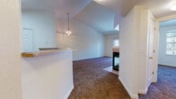 Located at 702 W Belleview Ave in Littleton, Colorado, this single-floor home offers a well-designed open-concept layout that seamlessly connects the living, dining, and kitchen areas. The living room is a standout space, featuring soaring vaulted ceilings that create an airy, expansive feel, complemented by a stylish pendant chandelier. A tile-surround fireplace serves as a natural focal point, adding warmth and character to the room. Sliding glass doors provide natural light and outdoor access. Plush carpeting runs throughout the main living and bedroom areas, while tile flooring defines the kitchen and entryway. The kitchen is equipped with light wood cabinetry reaching the upper walls, laminate countertops, a peninsula with a sink, and white appliances including a refrigerator and electric range. A pass-through counter connects the kitchen to the dining area, enhancing the open flow. The bedroom features a large window overlooking mature trees, filling the room with natural light and peaceful views. The bathroom includes a tiled tub-and-shower combination with a classic white and tan tile design. The home's clean, neutral palette throughout provides a versatile canvas ready for personalization.
