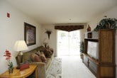 This single-floor residence offers a comfortable and practical layout across several well-defined living spaces. The living room is bright and welcoming, featuring plush carpet, a sliding glass door that fills the room with natural light and provides views of the outdoors, and ample space for seating and entertainment. Adjacent to the living area, a dedicated dining space accommodates a full dining table and chairs beneath recessed lighting, ideal for everyday meals or entertaining guests.

The galley-style kitchen is efficiently designed with warm wood cabinetry lining both sides, white appliances including a refrigerator, range, dishwasher, and microwave, as well as hardwood-style flooring that adds a touch of warmth. A separate in-unit laundry area provides added convenience with a washer and dryer hookup and overhead shelving for storage.

The primary bedroom is generously sized with soft carpet, natural window light, and room for a full dresser and seating. The second bedroom comfortably fits two twin beds alongside a desk area, making it versatile for guests or additional occupants. Both bathrooms feature hardwood-style flooring, vanity cabinetry, and clean, neutral finishes throughout. The overall ambiance of the residence is warm and inviting, with consistent earth-tone accents tying each room together cohesively.