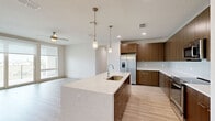 This well-appointed single-floor residence offers three bedrooms, two bathrooms, and a thoughtfully designed open-concept layout. The kitchen serves as a central feature, showcasing flat-front walnut-toned cabinetry extending to the ceiling, white quartz countertops, and a large center island with an undermount sink and pendant lighting overhead. Stainless steel appliances, including a side-by-side refrigerator and dishwasher, complement the contemporary aesthetic. Light wood-style flooring flows through the kitchen and living area, which is equipped with a ceiling fan and access to a private balcony through sliding glass doors, offering open outdoor views.

The spacious primary bedroom features large windows with scenic views and plush carpeting, while the additional bedrooms are similarly carpeted and naturally bright with oversized windows. Two closets provide ample storage, including a walk-in closet with dual hanging rods. The bathrooms feature large-format tile surrounds, soaking tubs, and wood-toned vanities with illuminated mirrors. A dedicated laundry room houses a full-size washer and water heater. Throughout, the design maintains a clean, modern palette of neutral tones.