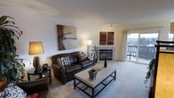 This single-floor residence centers around a welcoming living room that combines functionality with a warm, contemporary aesthetic. The space is anchored by a tile-surround fireplace, which serves as a natural focal point along one wall, adding both visual interest and a sense of coziness to the room. Plush wall-to-wall carpeting runs throughout the living area, contributing to a comfortable and inviting atmosphere.

Natural light fills the room through a large sliding glass door that opens to a private balcony, offering views of the surrounding outdoor landscape. The balcony provides an appealing extension of the living space, ideal for enjoying fresh air and outdoor scenery.

The living room is generously proportioned, easily accommodating a full seating arrangement, including a substantial sofa paired with a modern rectangular coffee table. Walls are painted in a clean, neutral tone, creating a versatile backdrop suited to a variety of décor styles. Recessed and track lighting supplements the natural light, ensuring the space remains well-illuminated throughout the day. Overall, the layout feels open, organized, and thoughtfully designed for comfortable single-level living.