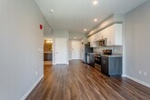 Located at 1409 E Meyer Blvd in Kansas City, Missouri, this single-floor unit presents a thoughtfully designed contemporary layout with a cohesive aesthetic carried throughout each space. The open living and kitchen area serves as the heart of the unit, where rich, dark hardwood-style flooring extends across the main living zones, complementing the neutral gray walls and white trim for a clean, modern look.

The kitchen is well-appointed with a full suite of stainless steel appliances, including a refrigerator, electric range, built-in microwave, and dishwasher. Dark wood cabinetry on the lower portion contrasts neatly with bright white upper cabinets, while granite countertops and a stainless steel sink add a polished finish. Recessed lighting illuminates the space effectively. A dedicated closet adjacent to the kitchen houses a stacked washer and dryer, providing the convenience of in-unit laundry.

The bedroom is carpeted for comfort and benefits from a window that brings in natural light and outdoor views, paired with a ceiling fan overhead. Access to a closet and the bathroom is conveniently located within the bedroom area. The bathroom features subway tile in the shower, light flooring, and a straightforward, functional design with neutral tones throughout.