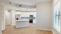 Located in Bonita Springs, Florida, this well-appointed three-bedroom, three-bathroom residence offers a thoughtfully designed single-floor layout. The open-concept living, dining, and kitchen area serves as the heart of the home, featuring light wood-look flooring, neutral toned walls, and generous natural light through large windows and glass doors. The kitchen is outfitted with white shaker-style cabinetry, a light blue tile backsplash, stainless steel appliances including a French door refrigerator and range, and a center island with white quartz countertops, accented by modern pendant lighting. The living area opens to a patio through a glass door, extending the living space outdoors. The three bedrooms are carpeted and each features a ceiling fan, patio access, and ample closet space among the six total closets throughout the home. The bathrooms are finished with white cabinetry, quartz countertops, large mirrors, and tiled tub-shower combinations with wood-look flooring. Two hallways connect the rooms efficiently, while an attached private garage provides secure parking and additional storage with a concrete floor and direct interior access.