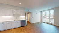 Located at 540 21st St in Oakland, CA, this modern single-floor unit offers a clean, contemporary design with an open-concept layout that seamlessly connects the kitchen and living area. The kitchen is well-appointed with sleek white flat-panel cabinetry extending to the ceiling, stainless steel appliances including a refrigerator, electric range, built-in microwave, and dishwasher, all complemented by light countertops and warm hardwood-style flooring. A large floor-to-ceiling window in the living area fills the space with natural light and frames views of the surrounding Oakland cityscape.

The unit includes two bedrooms, both finished with plush wall-to-wall carpeting and large windows that invite ample daylight. One bedroom provides direct access to a full bathroom featuring a shower-tub combination with white tile surround, hardwood-style flooring, and a white vanity. A second bathroom offers a walk-in glass-enclosed shower and hardwood-style flooring, providing a clean and functional design. The crisp white walls throughout the unit enhance the bright, airy ambiance, while recessed lighting adds a polished, modern feel. The overall aesthetic is minimal and contemporary, ideal for urban living in the heart of Oakland.