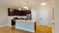 Located at 100 Holling FR in Frederick, MD, this single-floor residence offers a thoughtfully designed layout that balances functionality and modern style. The kitchen is a standout feature, showcasing rich dark espresso cabinetry, a classic white subway tile backsplash, stainless steel appliances including a gas range, microwave, and refrigerator, and a generous island topped with light granite countertops. Light hardwood-style flooring runs throughout the kitchen and living areas, lending warmth and continuity to the open-concept floor plan. The expansive living area provides ample room for various furniture arrangements and is bathed in a warm, neutral palette with crown molding accents that add a refined touch. The bedroom is carpeted for comfort, features a window that invites natural light, and connects seamlessly to the rest of the unit. The full bathroom is finished with a dark wood vanity, white countertop, tiled tub-shower combination, and elegant brushed nickel fixtures. Throughout the space, clean white trim, neutral walls, and well-placed lighting create a bright, inviting ambiance suited for everyday living.