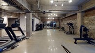Located at 900 Third Ave N in downtown Nashville, this fitness facility combines industrial architectural character with a full suite of professional-grade workout equipment. The space is defined by its raw, urban aesthetic: exposed concrete ceilings with visible ductwork and conduit, original stone and brick accent walls, and polished concrete flooring throughout. Structural concrete columns punctuate the open floor plan, reinforcing the building's historic industrial identity.

The facility is organized into distinct training zones across its expansive single-level layout. A dedicated strength area features cable machines, a multi-functional power rack with accessory storage, a dumbbell rack, barbell tree, and flat benches. A large open floor zone accommodates functional training, with battle ropes and a heavy tire available for conditioning work. The cardio section is well-appointed with treadmills, rowing machines, and stationary spin bikes. A boxing area includes a suspended heavy bag and speed bag station. Mirrored walls in select zones enhance spatial depth and support form monitoring. Track lighting provides focused illumination throughout, creating a purposeful and energetic training environment suited for a wide range of fitness disciplines.