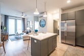 This thoughtfully designed single-floor residence offers a seamless blend of modern aesthetics and functional living. The open-concept layout connects the kitchen and living area, creating a bright and welcoming communal space. Light hardwood-style flooring runs throughout, complementing the clean white walls and contemporary finishes.

The kitchen is a standout feature, showcasing charcoal grey shaker-style cabinetry, white quartz countertops, and a full suite of stainless steel appliances including a large refrigerator, gas range, and built-in microwave. A central island with bar seating and pendant lighting above serves as both a prep space and casual dining area, while under-cabinet lighting and a subway tile backsplash add refined detail.

The living area is generously proportioned, with large windows fitted with blinds that allow for ample natural light. A ceiling fan adds comfort to the space.

Two bedrooms provide comfortable retreats, each featuring ceiling fans, large windows, and plush carpeting. The primary bedroom is distinguished by a bold navy accent wall, creating a striking backdrop for the room.

Two bathrooms serve the residence. One features a soaking tub with full tile surround and an illuminated vanity mirror, while the other offers a walk-in glass-enclosed shower with marble-style tile. Both bathrooms share the same grey cabinetry and white countertop palette found throughout the home.
