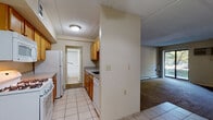Located at Chelsea Ridge Mall in Wappingers Falls, NY, this single-floor residence offers a functional and straightforward layout. The galley-style kitchen is equipped with warm wood cabinetry, a gas range, built-in microwave, dishwasher, and a full-size refrigerator. Light ceramic tile flooring runs throughout the kitchen and entry areas, providing a clean, practical surface. A pass-through counter connects the kitchen to the adjacent living space, creating an open feel between the two areas. The living room is carpeted and centered around a fireplace, adding a cozy focal point to the space. A wall-mounted air conditioning unit and baseboard heating provide year-round climate control. Large sliding glass doors allow natural light to fill the room and offer views of the surrounding greenery. A ceiling fan is present in the entryway or adjoining area, enhancing airflow throughout. The bedroom also features plush carpeting and its own sliding glass doors that open to outdoor views, bringing in abundant natural light. The bathroom is finished with neutral tile flooring, a white vanity with ample cabinet storage, and a tub/shower combination with grab bars and a curved curtain rod.
