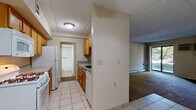 Located at Chelsea Ridge Mall in Wappingers Falls, NY, this single-floor residence offers a functional and straightforward layout. The galley-style kitchen is equipped with warm wood cabinetry, a gas range, built-in microwave, dishwasher, and a full-size refrigerator. Light ceramic tile flooring runs throughout the kitchen and entry areas, providing a clean, practical surface. A pass-through counter connects the kitchen to the adjacent living space, creating an open feel between the two areas. The living room is carpeted and centered around a fireplace, adding a cozy focal point to the space. A wall-mounted air conditioning unit and baseboard heating provide year-round climate control. Large sliding glass doors allow natural light to fill the room and offer views of the surrounding greenery. A ceiling fan is present in the entryway or adjoining area, enhancing airflow throughout. The bedroom also features plush carpeting and its own sliding glass doors that open to outdoor views, bringing in abundant natural light. The bathroom is finished with neutral tile flooring, a white vanity with ample cabinet storage, and a tub/shower combination with grab bars and a curved curtain rod.