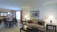 This two-floor residential space offers a comfortable and functional layout designed for everyday living. The living area is finished with soft wall-to-wall carpeting and painted in neutral tones that create a warm, inviting atmosphere throughout. A large window dressed with decorative rust-colored curtains allows natural light to brighten the room, contributing to an open and airy feel.

The living room is thoughtfully arranged with ample space for seating and relaxation. A cushioned sofa with accent pillows serves as the focal point of the room, complemented by a dark wood coffee table and a side table with a classic table lamp that adds a soft, ambient glow. Framed artwork on the wall adds a finishing touch to the clean, understated décor.

Adjacent to the living room, the dining area accommodates a dark wood table and chairs, making it ideal for everyday meals or casual gatherings. The open flow between the living and dining spaces enhances the sense of roominess and connectivity within the home.

Overall, the space presents a tidy, well-maintained interior with a neutral color palette, practical furnishings, and a layout that balances comfort with functionality across two floors.