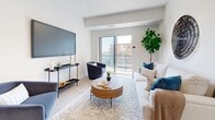 This thoughtfully designed 2-bedroom, 2-bathroom residence spans a single floor and delivers a clean, contemporary aesthetic throughout. Light-toned hardwood flooring flows seamlessly from room to room, complementing the crisp white walls and creating a bright, airy atmosphere.

The open-concept kitchen and living area serves as the heart of the home. The kitchen features white shaker-style cabinetry, white quartz countertops, a tile backsplash, and a full suite of stainless steel appliances including a range, over-the-range microwave, dishwasher, and refrigerator. A kitchen island with bar seating provides additional workspace and casual dining options.

The living room is generously proportioned, bathed in natural light from large sliding glass doors that open onto a private balcony with urban views. Both bedrooms are comfortably sized, with the primary bedroom offering a spacious layout, large windows with outdoor views, and light-filled interiors. The second bedroom similarly benefits from natural light through its own window.

Both bathrooms are finished in a clean, all-white palette, each featuring a tub-shower combination and a vanity with ample storage. A dedicated laundry room houses a full-sized washer and dryer, adding everyday convenience. The overall ambiance is modern, bright, and functional.