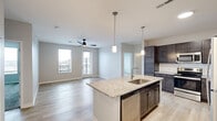 This thoughtfully designed 2-bedroom, 2-bathroom residence spans a single floor and delivers a seamless blend of modern aesthetics and functional living. The open-concept kitchen and living area serves as the heart of the home, featuring rich dark-stained cabinetry, granite countertops, a subway tile backsplash, and a full suite of stainless steel appliances. A central island with an undermount sink and pendant lighting above anchors the space, flowing naturally into the bright living room equipped with a ceiling fan and light-toned hardwood-style flooring. Large windows and a glass door in the living area invite abundant natural light and provide access to a private balcony with views of the surrounding area. The primary bedroom is generously sized, complete with plush carpeting, a ceiling fan, and its own window for natural light. It connects to a well-appointed bathroom featuring dual granite-topped vanities, dark cabinetry, and ample storage. The second bedroom also offers carpeted flooring, a ceiling fan, and a large window with exterior views. Both closets are outfitted with wire shelving systems for organized storage. Light-toned luxury vinyl plank flooring unifies the main living areas, while neutral wall tones throughout create a clean, contemporary ambiance.