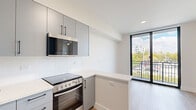 Studio 208 is a thoughtfully designed studio located in Miami, FL 33125, offering a clean, contemporary aesthetic throughout its efficiently planned single-floor layout. The open-concept design maximizes the use of space, seamlessly connecting the living area and kitchen into one cohesive environment.

The kitchen is a standout feature, outfitted with sleek gray flat-front cabinetry accented by matte black hardware, light quartz countertops, and a crisp white backsplash. Stainless steel appliances — including a built-in microwave, electric range with oven, and full-size refrigerator — provide full functionality. A peninsula counter extends the workspace and adds a natural division between the kitchen and living area.

The living space is bright and airy, benefiting from large black-framed sliding glass doors that open to a private balcony, offering views of the surrounding Miami cityscape and lush tree canopy. An additional window, fitted with a ceiling fan, further enhances natural light and ventilation throughout the space.

Light wood-tone luxury vinyl flooring runs throughout, complementing the neutral white walls and creating a warm, modern ambiance. A louvered closet and a teal-accented entry door add subtle design character. The overall atmosphere is clean, minimal, and move-in ready — well-suited for urban living in Miami.