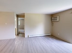 Located at 1640 S Greenfield Circle NE in Grand Rapids, this single-floor residence offers 670 square feet of practical living space across three bedrooms and one full bathroom. The open living room features durable light-toned laminate flooring, a wall-mounted AC unit, a baseboard heater, and a sliding glass door that opens to a private balcony overlooking a well-maintained lawn with mature trees. The adjacent kitchen is equipped with oak cabinetry, white countertops, a black electric range, a dishwasher, and a ceiling fan, providing ample storage and functionality. The three carpeted bedrooms each include ceiling fans with light fixtures and baseboard heating. The primary bedroom measures 150 square feet, while additional bedrooms offer closet space and natural light through windows with blinds. The full bathroom features a white tub-shower combo, wood-toned vanity cabinetry, and light wood-look vinyl flooring. Throughout the unit, neutral wall tones and consistent flooring create a cohesive, low-maintenance aesthetic. The property's green outdoor surroundings contribute to a calm residential atmosphere.