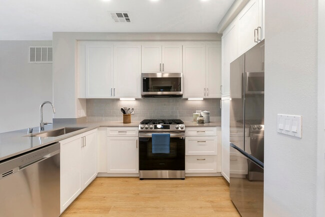 Renovated Package III kitchen with stainless steel appliances, grey quartz countertops, white cabinetry, grey tile backsplash, and hard surface flooring - Avalon Encino
