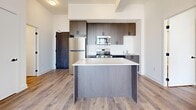Located at 2457 Old Bronte Rd in Oakville, Ontario, this modern 3-bedroom, 2-bathroom unit offers a thoughtfully designed single-floor layout with contemporary finishes throughout. Light wood laminate flooring flows seamlessly across every room, complementing the clean white walls and crisp trim that give the space a bright, airy feel.

The open-concept kitchen serves as the heart of the unit, featuring dark wood cabinetry that extends to the ceiling for ample storage, a white subway tile backsplash, a full suite of stainless steel appliances including a refrigerator, stove, microwave, and dishwasher, and a central island with a white countertop — ideal for both meal prep and casual dining. The kitchen opens directly into the living area, enhancing the sense of openness.

The primary bedroom is a comfortable size and benefits from generous natural light. The additional two bedrooms each feature large windows framing views of the surrounding Oakville skyline, with one room boasting a floor-to-ceiling window that floods the space with daylight. Each bedroom includes sliding-door closets for clean, efficient storage.

The bathrooms are finished in crisp white tile, with one featuring a soaker tub-shower combination. A dedicated laundry area and balcony round out this well-appointed unit, offering both practicality and outdoor access.