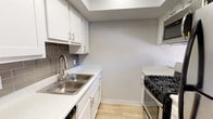 This two-floor space includes a thoughtfully designed kitchen that showcases a clean, modern aesthetic. White shaker-style cabinetry lines the walls, complemented by brushed nickel hardware and a gray subway tile backsplash that adds texture and visual interest. The countertops feature a white quartz-style surface, providing a bright and durable workspace. A stainless steel double-basin sink with a sleek pull-down faucet is positioned beneath the upper cabinets, maximizing functionality. Appliances include a black and stainless steel gas range and a stainless steel over-the-range microwave, offering a cohesive look throughout the kitchen. Light wood-tone flooring runs underfoot, contributing warmth to the otherwise crisp, neutral color palette. The walls are finished in a soft gray tone, creating a calm and contemporary ambiance. The layout is efficiently organized, with ample cabinetry for storage both above and below the counter. The overall design of the kitchen balances practicality with modern style, making it a functional and visually appealing space within this two-floor home.