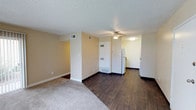This single-floor unit offers a practical and comfortable layout designed for everyday living. The main living area is a highlight of the space, combining plush carpet and dark hardwood-style flooring that visually defines separate zones. Warm beige walls and a textured ceiling run throughout, creating a consistent and cozy ambiance. A ceiling fan provides added comfort, while a large sliding glass door floods the living area with natural light and offers a view of the greenery outside. The entry door opens directly into this open space, making the layout feel welcoming and connected.

The galley-style kitchen is efficiently arranged with white cabinetry, dark granite-look countertops, and dark hardwood-style flooring. It is equipped with a gas range and a dishwasher, with ample cabinet storage lining both sides of the corridor layout.

The bedroom is a quiet, carpeted room with a large window dressed with vertical blinds, allowing for adjustable natural light. The textured ceiling continues here, maintaining a uniform aesthetic throughout the unit.

The bathroom features a full-size soaking tub and shower combo with a curved curtain rod and clean white surround, complemented by brushed nickel fixtures and a coordinating towel bar, offering a simple yet functional design.