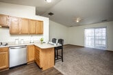 This single-floor unit is designed with an open-concept layout that connects the kitchen, dining, and living areas into one cohesive space. The kitchen is well-equipped with warm oak cabinetry, stainless steel appliances including a refrigerator, range, and dishwasher, and light countertops that extend into a peninsula with bar seating — ideal for casual dining or entertaining. Wood-style flooring runs throughout the kitchen and transitions into plush carpeting across the living and dining areas.

The living area benefits from vaulted ceilings that enhance the sense of openness, along with a ceiling fan and a sliding door that provides access to an outdoor patio and brings in natural light. A dedicated in-unit laundry closet accommodates a full-sized washer and dryer, adding everyday convenience.

The bedrooms are carpeted and feature neutral walls, wood-trimmed doors, and closets with built-in shelving for organized storage. One bedroom includes a window with vertical blinds, allowing for natural light. The bathroom is finished with oak cabinetry, a wide vanity mirror, light countertops, wood-style flooring, and a shower-tub combination. Overall, the unit offers a functional and comfortable layout with consistent, neutral finishes throughout.