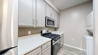 Located at 14110 Big Crest Lane in Woodbridge, VA, this well-appointed one-bedroom, one-bathroom residence offers a thoughtfully designed single-floor layout with a clean, modern aesthetic throughout. Neutral warm-toned walls and light-colored luxury vinyl plank flooring run through the main living areas, creating a bright and cohesive atmosphere.

The living room is a comfortable, open space anchored by a ceiling fan and sliding glass doors that lead to a private balcony, allowing natural light to fill the room and providing pleasant outdoor views. The kitchen is efficiently laid out with gray shaker-style cabinetry, quartz countertops, and stainless steel appliances including a gas range, over-the-range microwave, and dishwasher. A stacked washer and dryer unit is conveniently tucked within the kitchen area, offering in-unit laundry.

The bedroom features plush wall-to-wall carpeting, a ceiling fan, and a window with outdoor views, creating a quiet and comfortable retreat. A dedicated closet provides ample storage. The bathroom is finished with wood-look tile flooring, a white vanity with granite countertop, and a full tub-shower combination with tiled surround and chrome fixtures. A hallway connects the rooms, completing this efficient and move-in-ready home.