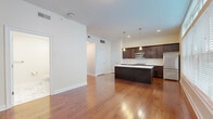 Located at 233 Lake Ave in Saratoga Springs, NY, this well-appointed one-bedroom, one-bathroom residence offers a smart, efficient layout across a single floor. The open-concept living and kitchen area serves as the heart of the space, highlighted by rich hardwood flooring and a large multi-pane window that floods the room with natural light. The kitchen is a standout feature, showcasing dark espresso cabinetry, white quartz countertops, stainless steel appliances including a refrigerator, microwave, and range, and a center island with an undermount sink illuminated by stylish pendant lighting. The living area flows seamlessly from the kitchen, creating an inviting space ideal for both everyday living and entertaining. The bedroom is carpeted for comfort and benefits from its own window, maintaining a bright and airy feel. A well-organized walk-in closet with built-in shelving, hanging rods, and a drawer unit provides generous storage. The bathroom features elegant marble-style tile flooring, a dark-toned vanity, and clean white walls, contributing to a polished, modern aesthetic throughout. The overall ambiance is contemporary and clean, with neutral tones creating a cohesive and welcoming environment.