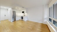 Located at 1975 Boulevard de Maisonneuve Ouest in Montréal, this studio offers a well-organized, single-floor layout that maximizes every square foot with a clean, modern aesthetic throughout. Light hardwood flooring runs continuously across the main living areas, lending warmth and cohesion to the space.

Upon entry, a dedicated entrance leads into the heart of the studio. The open-concept kitchen is a standout feature, outfitted with sleek, handleless white cabinetry, stainless steel appliances including a full-size refrigerator, a built-in microwave, and a stainless range. Recessed lighting illuminates the kitchen's bright white surfaces, creating a crisp, contemporary look.

The living area is generously proportioned for a studio and benefits from large floor-to-ceiling windows that flood the space with natural light. A glass door provides direct access to a balcony, connecting the interior to the outdoors. The white walls and clean lines throughout contribute to an airy, open ambiance.

The bathroom is finished with large-format beige stone-look tiles on both the floor and accent wall, paired with a white floating vanity and a mirrored cabinet above. A glass-enclosed shower completes the space. A closet provides additional storage. The overall design is minimal, functional, and move-in ready.