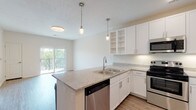 This single-floor residence offers a clean, modern aesthetic throughout, anchored by an open-concept kitchen and living area designed for both functionality and comfort. The kitchen is a standout feature, showcasing white shaker-style cabinetry with open display shelving, granite-patterned countertops, and a full suite of stainless steel appliances including a refrigerator, electric range, over-the-range microwave, and dishwasher. A peninsula island with an undermount double sink serves as a natural gathering point, while pendant lighting adds a polished finishing touch overhead. Light wood-style flooring runs through the kitchen and living areas, creating a cohesive, contemporary feel.

The living space opens directly to a balcony through a sliding glass door, allowing natural light to flow generously into the interior. The bedroom features plush carpeting, a wide window with treetop views, and a ceiling fan. A spacious walk-in closet with multi-tier wire shelving provides ample storage. The bathroom is finished with granite-top vanity cabinetry, a undermount sink, wood-look flooring, and a full soaking tub. Throughout, the neutral color palette and consistent finishes create a bright, welcoming ambiance.